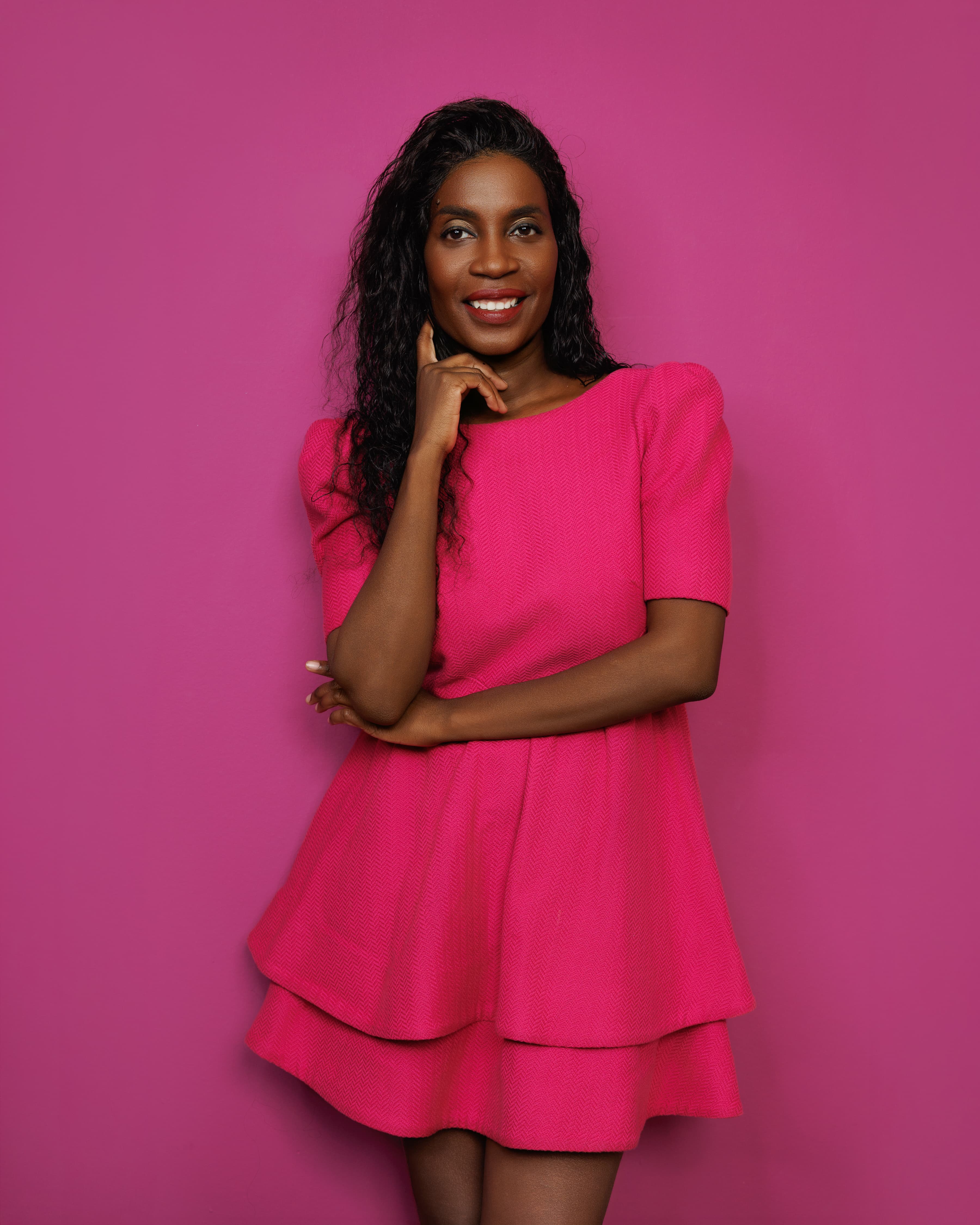 A smiling woman in a vibrant pink dress posing against a matching background.
